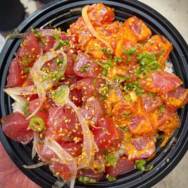 A black bowl filled with two types of poke, one with onions and sesame seeds.