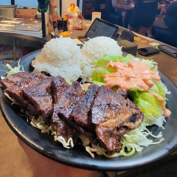 Grilled short ribs with rice and a side salad with dressing on a black plate.