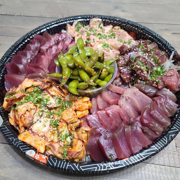 A large platter of various poke, including tuna, octopus, and edamame, on a wooden table.